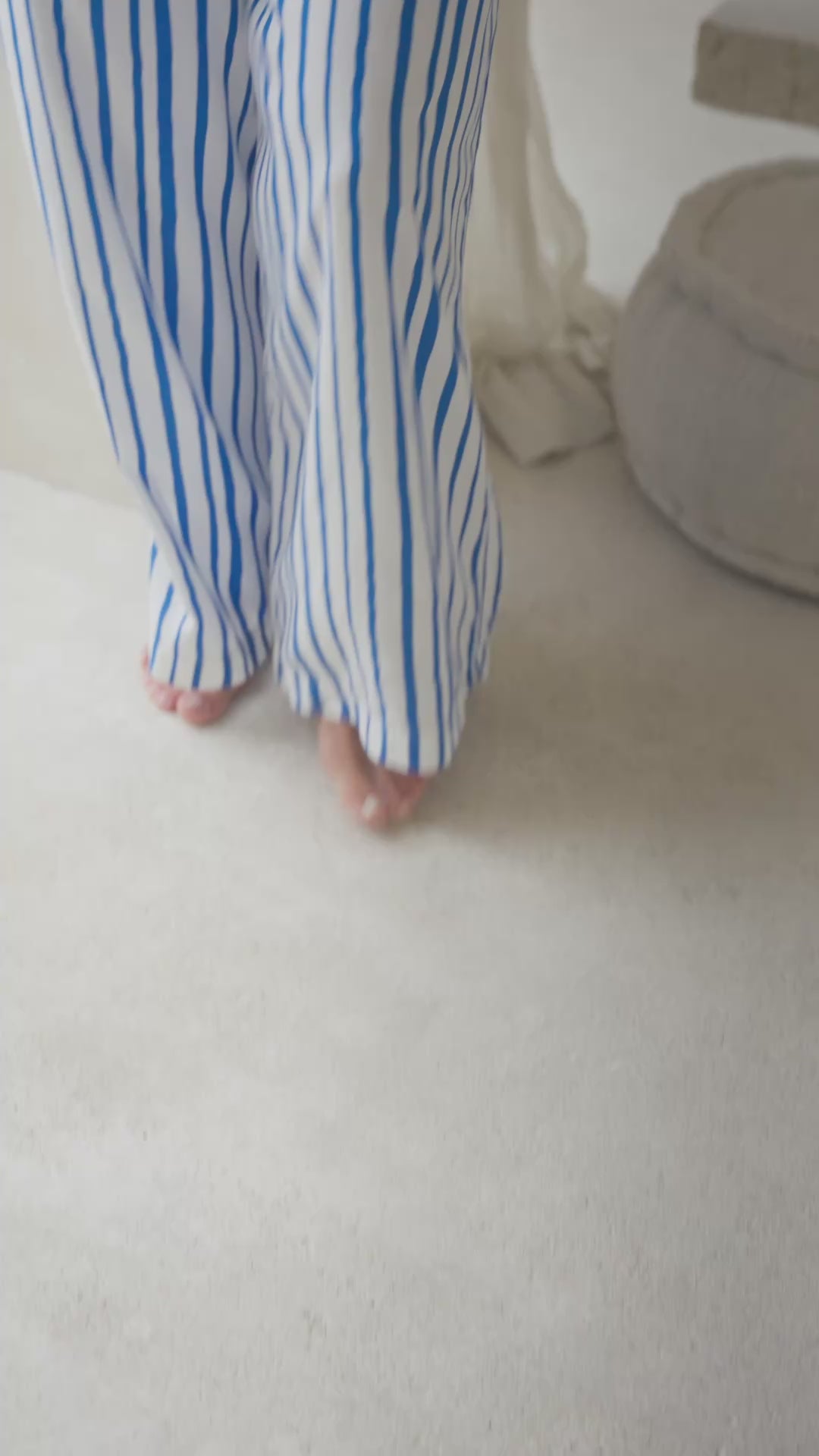 Load video: Woman wearing a white tank top and blue striped pants in a softly lit room