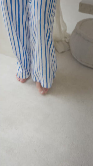 Woman wearing a white tank top and blue striped pants in a softly lit room