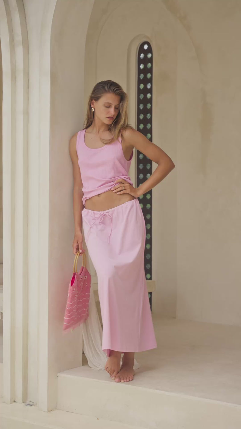 Woman wearing a pink maxi skirt and tank top in a marble courtyard setting.