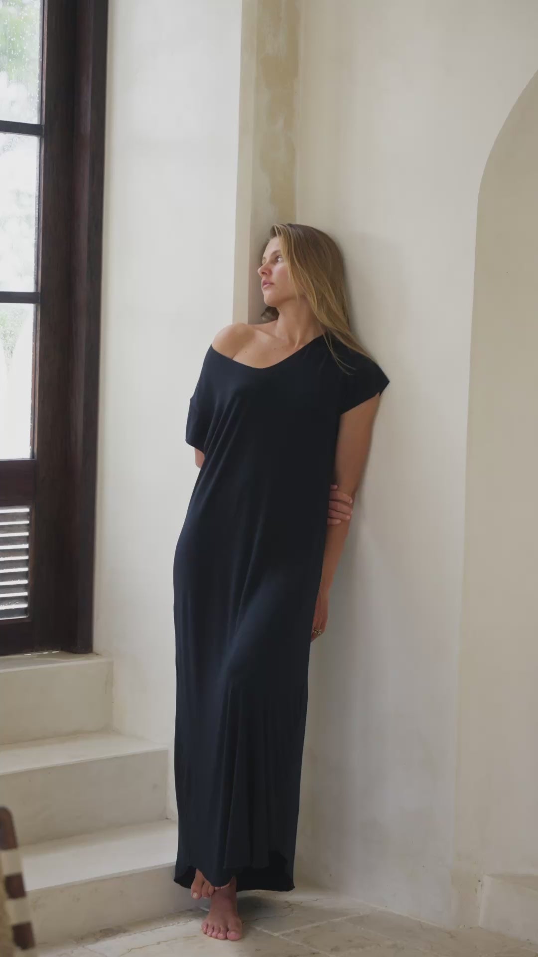 Load video: Woman in a black maxi dress standing  in a bright room.