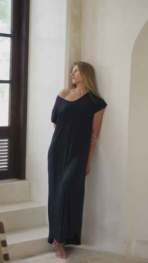 Woman in a black maxi dress standing  in a bright room.