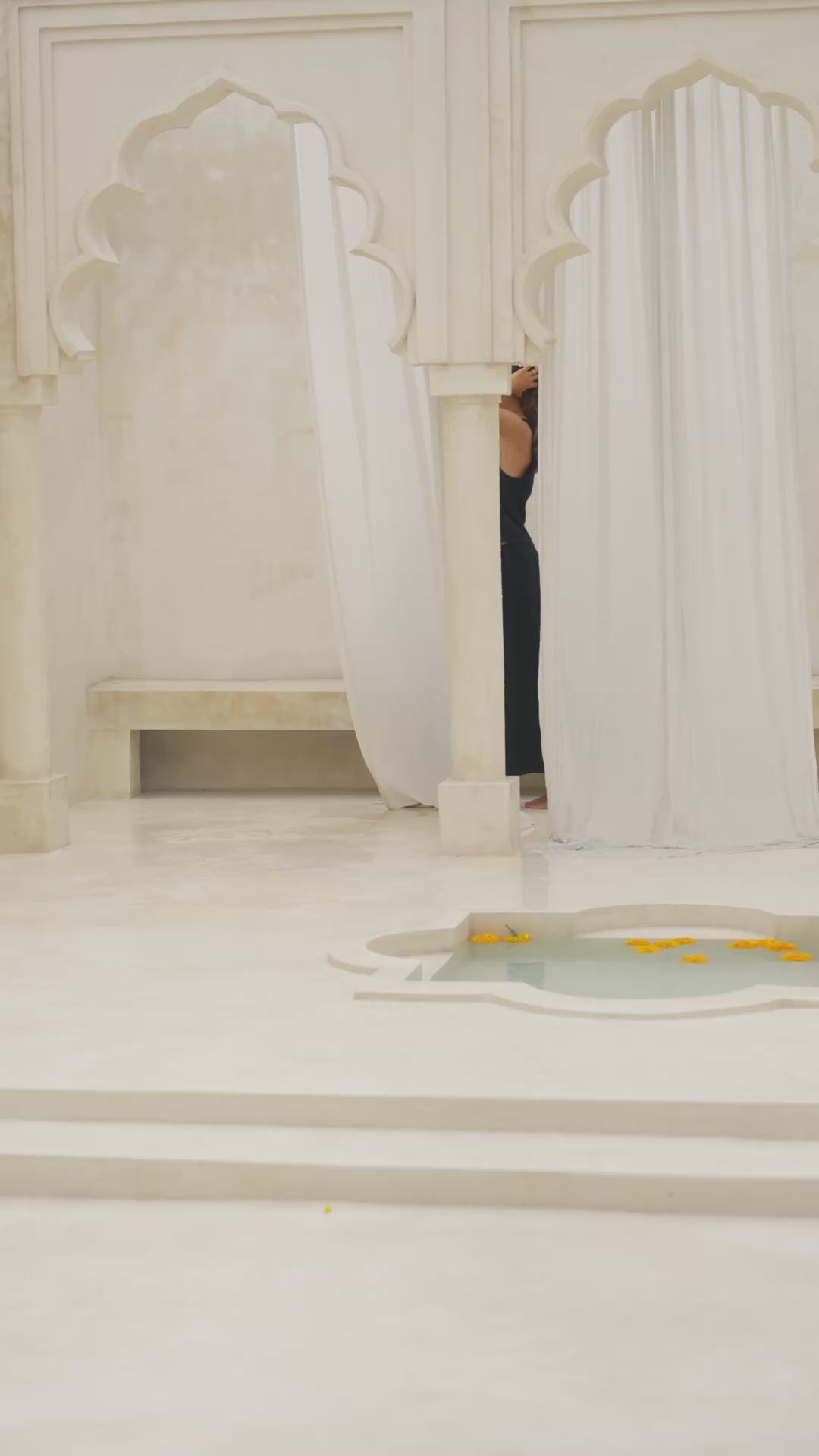Load video: Woman wearing a black maxi skirt and tank top in a marble courtyard setting.