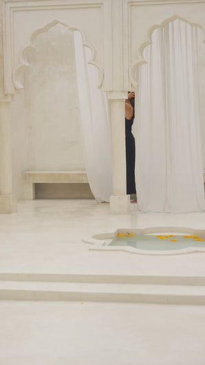Woman wearing a black maxi skirt and tank top in a marble courtyard setting.