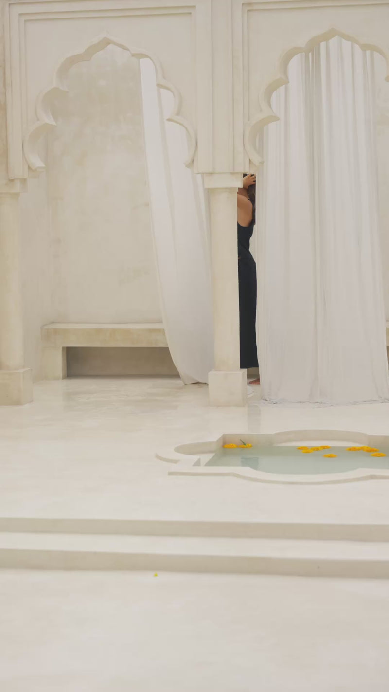 Woman wearing a black maxi skirt and tank top in a marble courtyard setting.