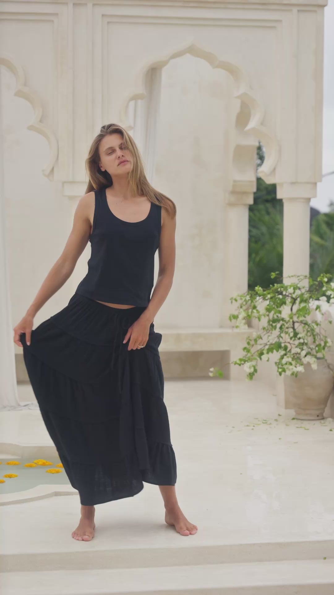 Load video: Woman wearing a black tiered skirt and tank top in a marble interior setting