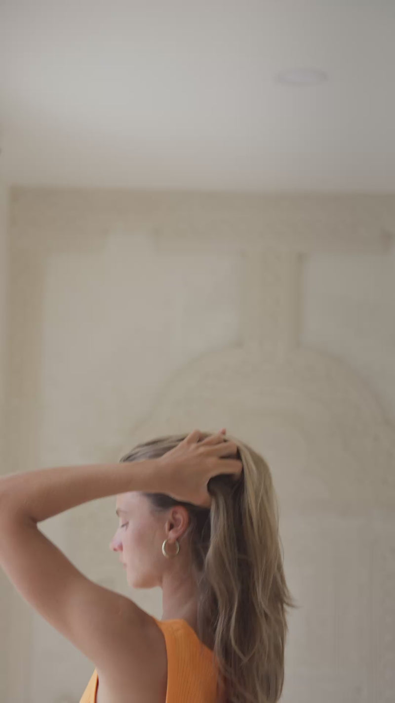 Woman wearing an orange tank top and striped pants in a softly lit room.