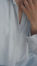 Load and play video in Gallery viewer, Woman wearing a light blue shirt over  a white tank top sitting against a neutral wall.

