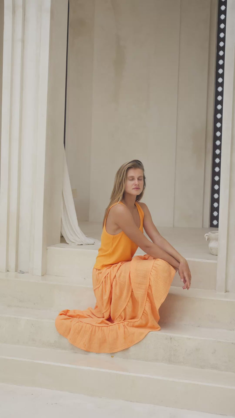 Woman in an orange skirt and tank top sitting on steps  in front of a classical architectural archway.
