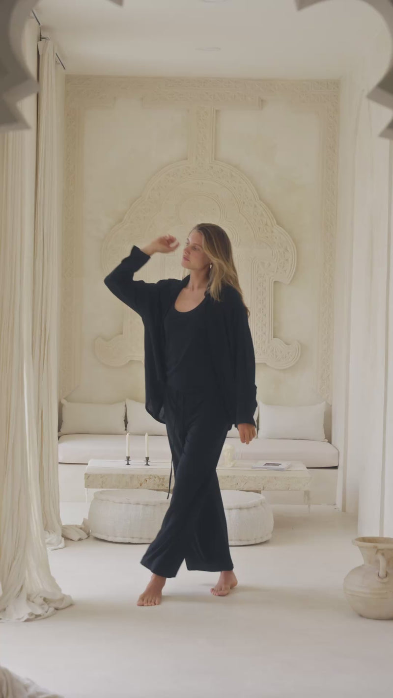 Woman in a black shirt, tank top and pants standing in a luxurious room with white decor