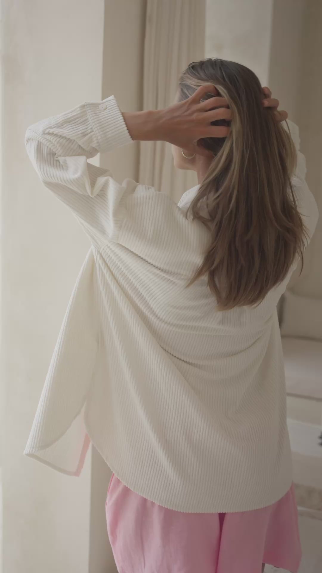 Load video: Woman wearing a white corduroy shirt and pink shorts against a neutral background
