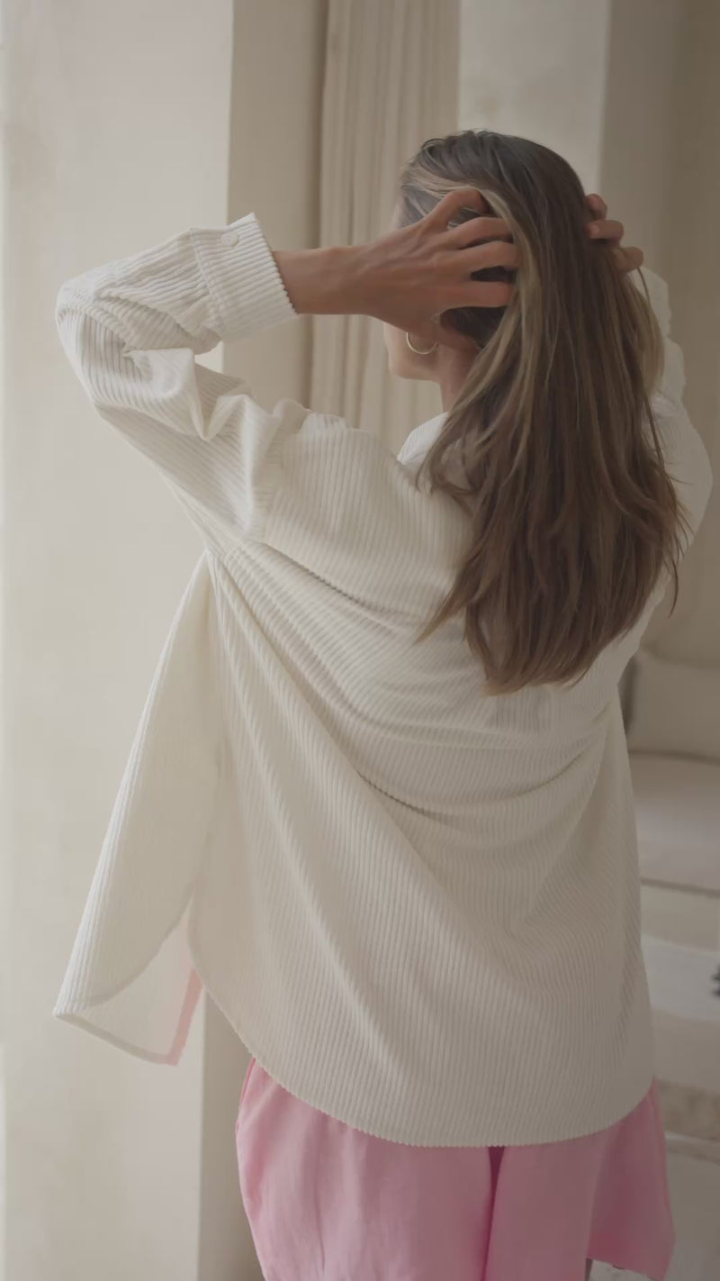 Woman wearing a white corduroy shirt and pink shorts against a neutral background